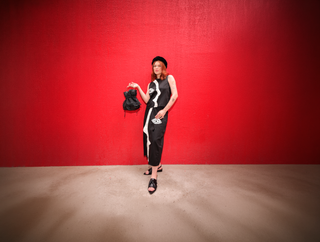 Savana Sá, em fundo vermelho, com a Bolsa Bucket de Couro e Sandália de Couro da Collab